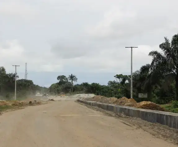 Wide cleared road with a partly built drain wall, on the Ikot Akpaden-Okoroete-Iko Road.