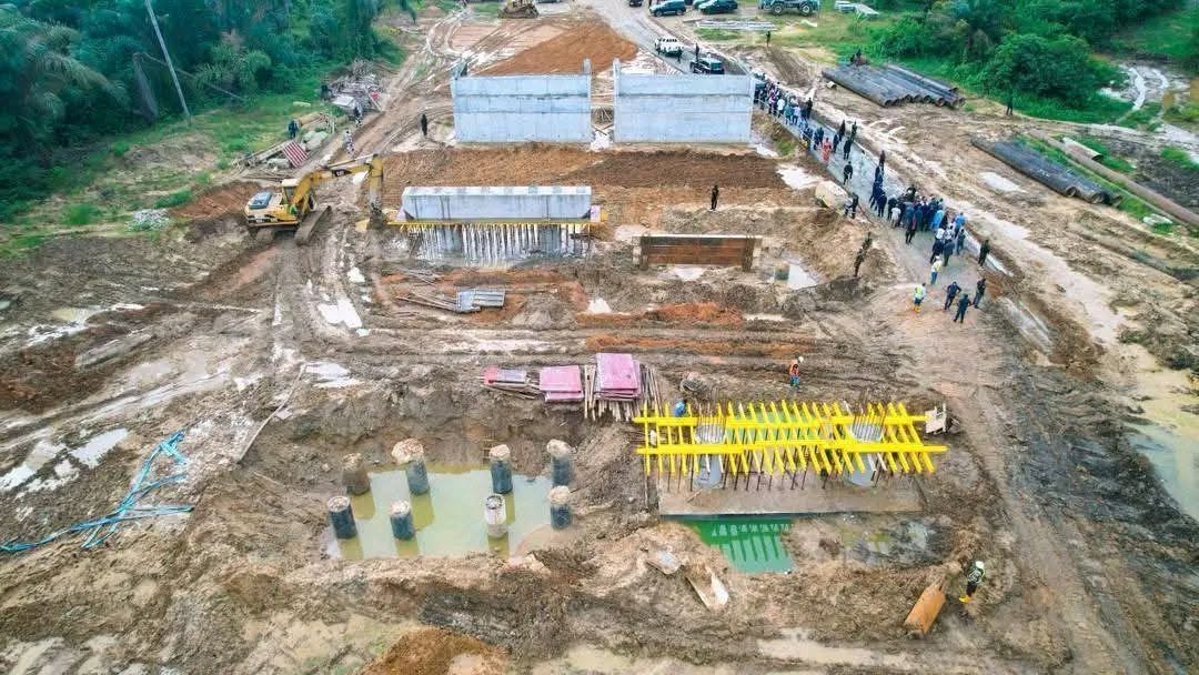 Drone view of concrete pile caps and a bridge beam on formwork at the Ofriyo river crossing, with abutment walls beyond