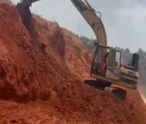 Excavator cutting into a red earth slope along the road route