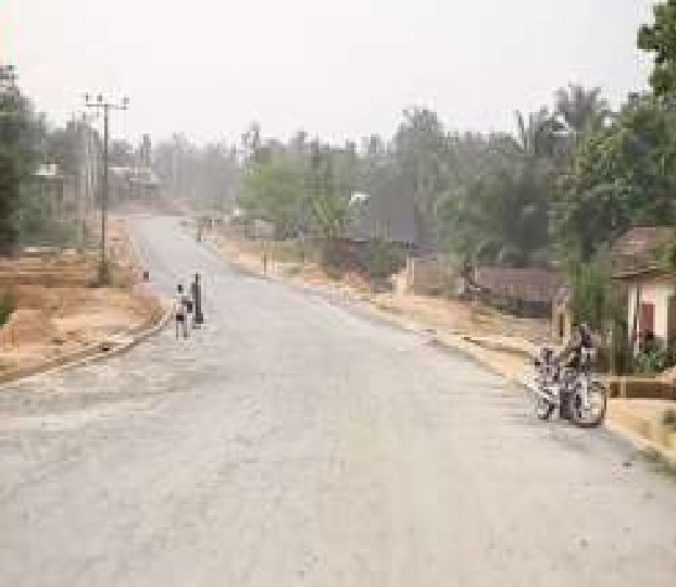Wide graded road with gravel base passing through a village