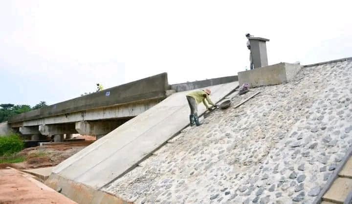 Bridge beams in place with a worker pitching the stone slope of the approach embankment