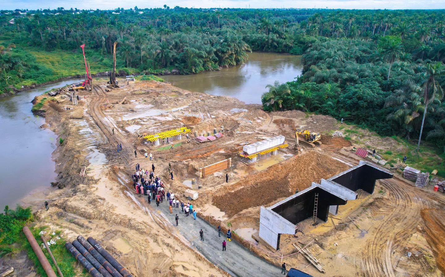Aerial view of bridge works beside the river, with abutment walls and stacked pipes