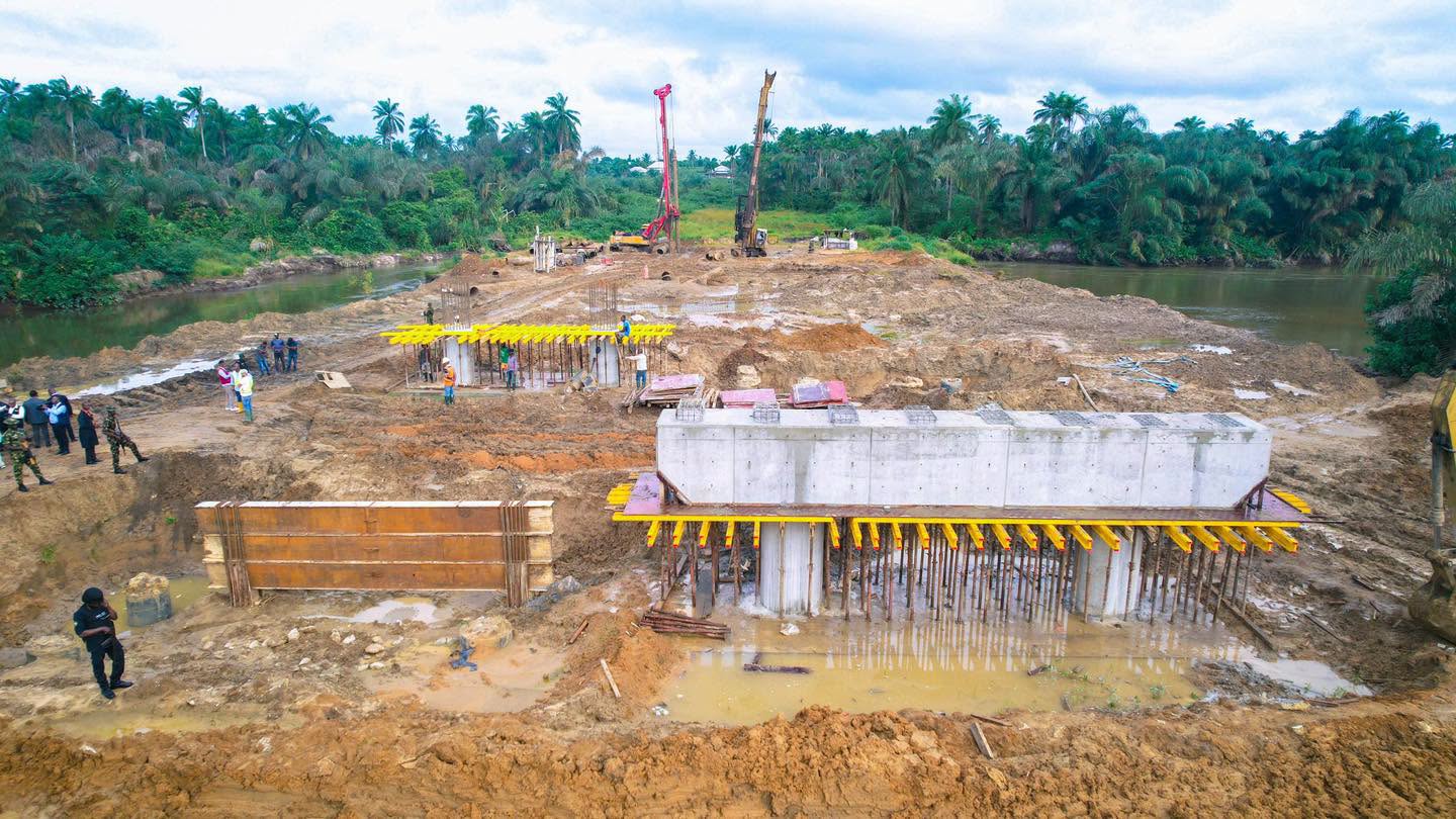 Concrete bridge beam on formwork at the site, with piling rigs in the distance