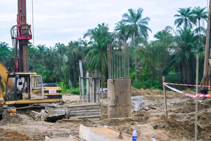 Bridge pier column with exposed reinforcement bars beside a piling rig and tracked machine at the river site