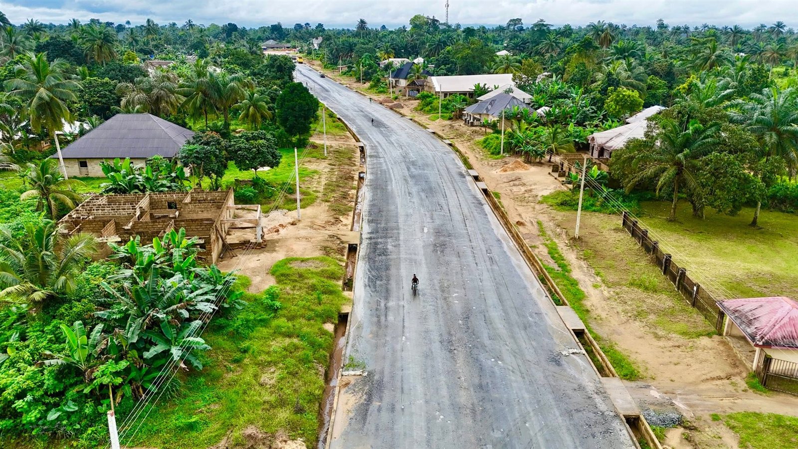 Drone view of the new dual carriageway with a first asphalt layer, kerbs and side drains through a village