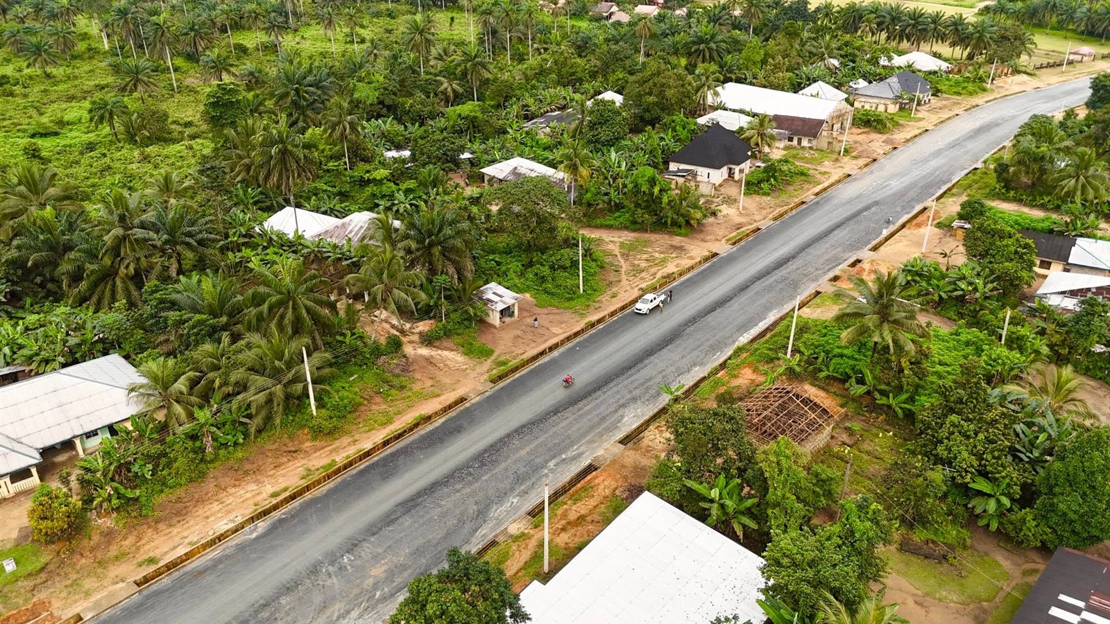 Angled drone view of the asphalt carriageway with side drains and houses along the route