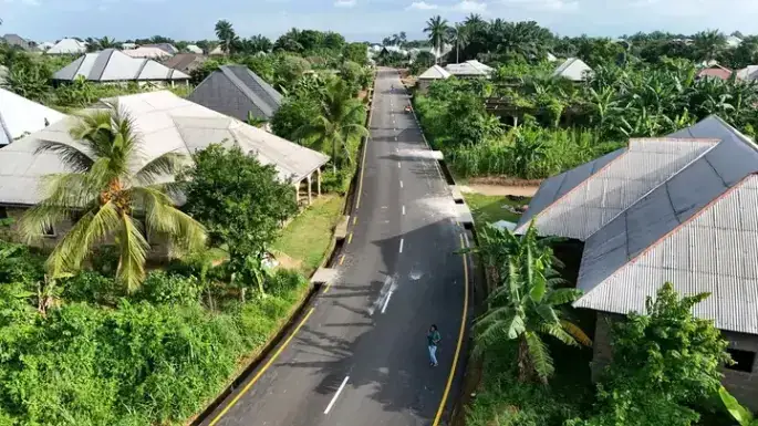 Aerial view of a surfaced road with drain edges and buildings alongside, Oron.